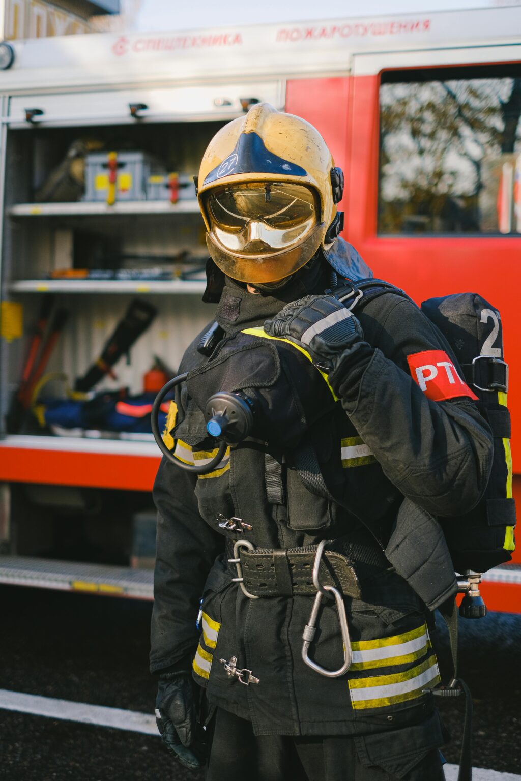 Firefighter in reflective uniform ready for action by a fire truck.