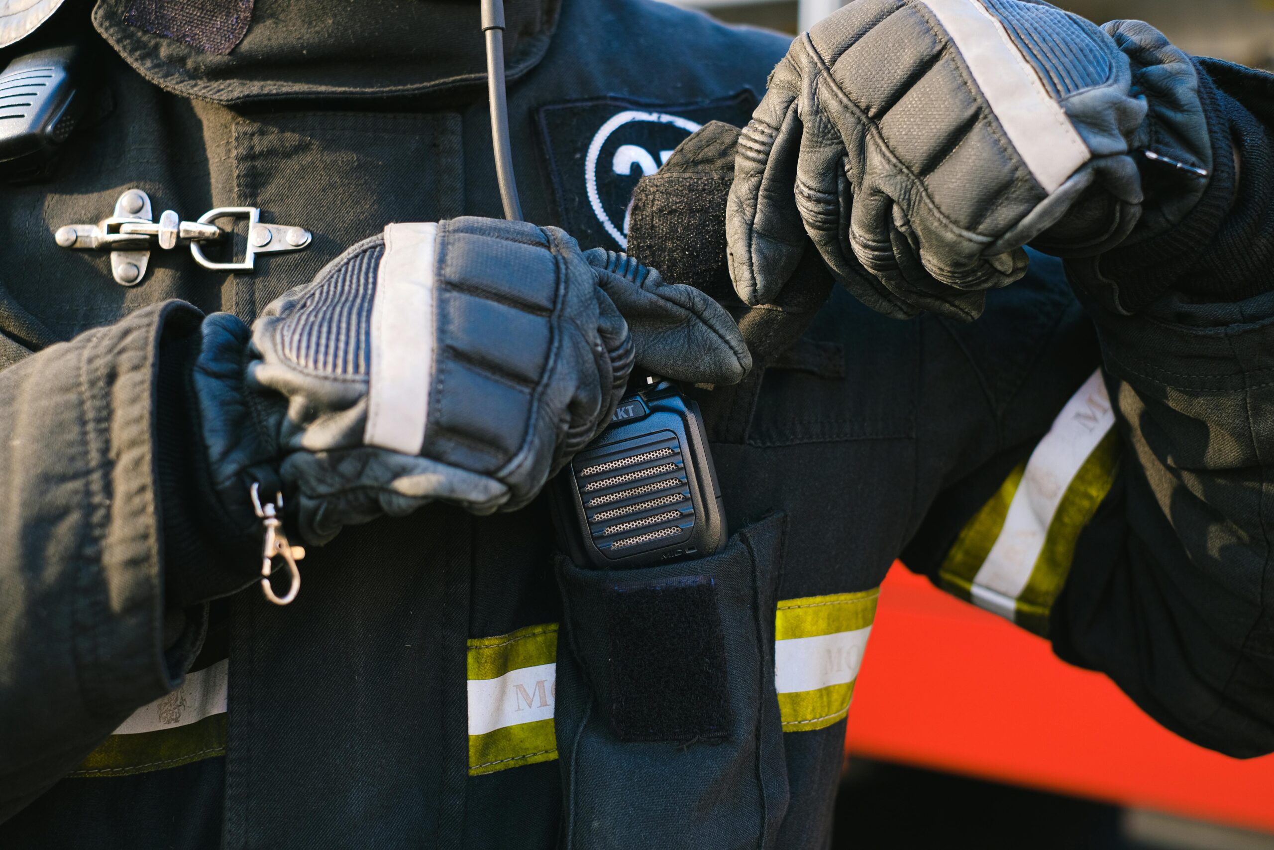 Close-up of a firefighter using a transceiver with gloved hands for communication.