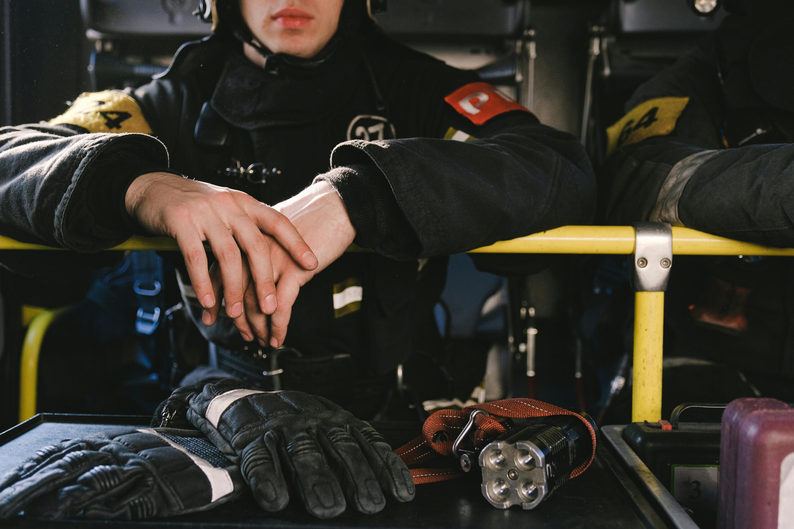 A firefighter in uniform rests inside a vehicle with gear including gloves and flashlight.